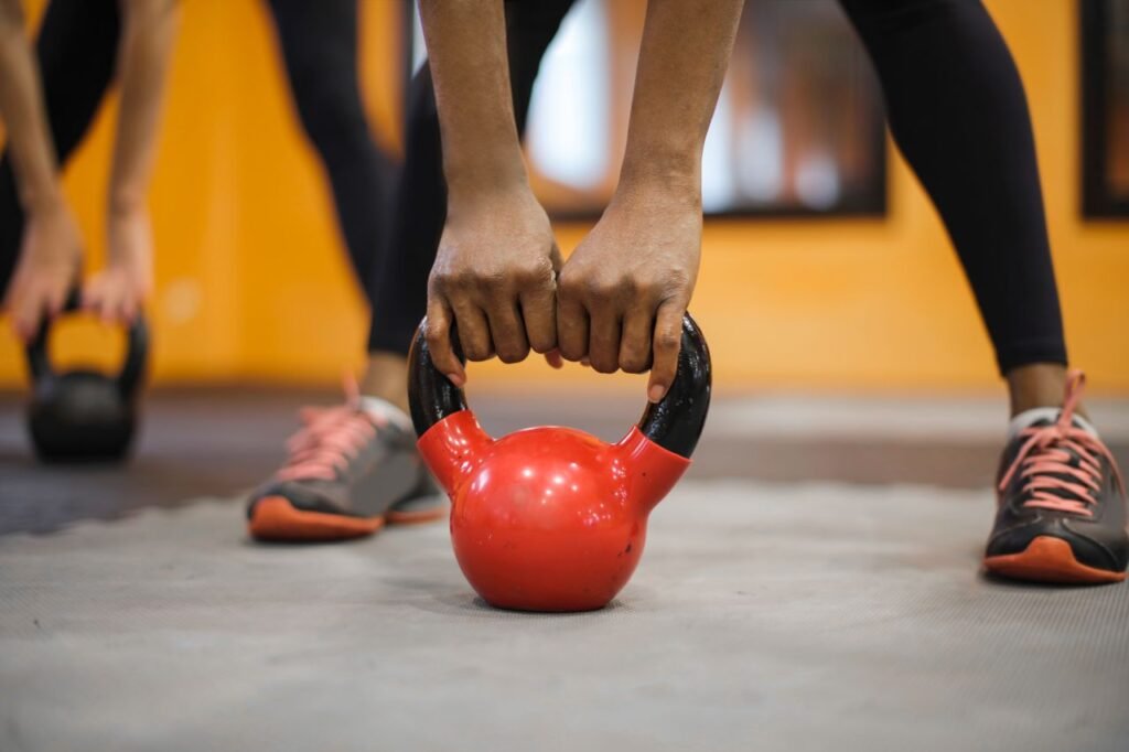 Close-up of hands gripping a red kettlebell in a vibrant indoor gym setting.